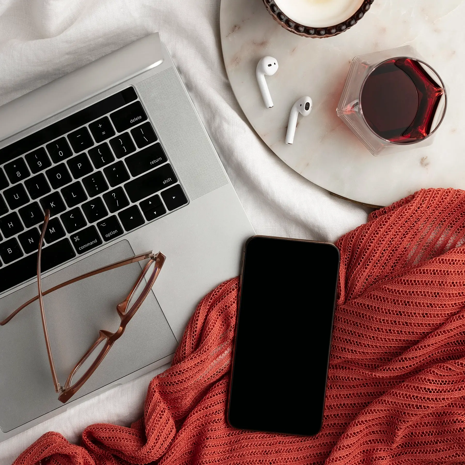 laptop with glasses and iPhone with a red blanket